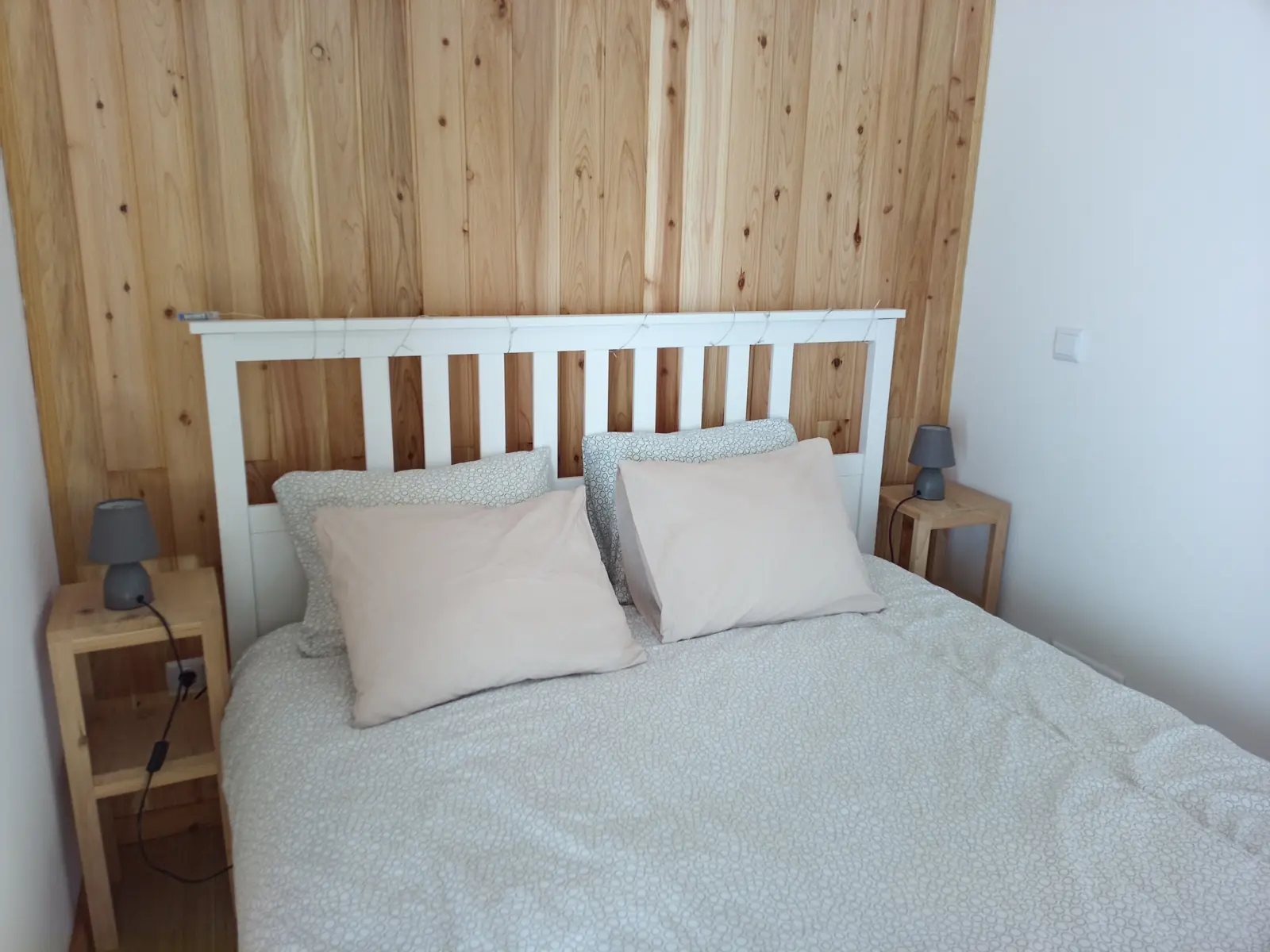 Doppelbett vor einer Wand aus hellem Holz