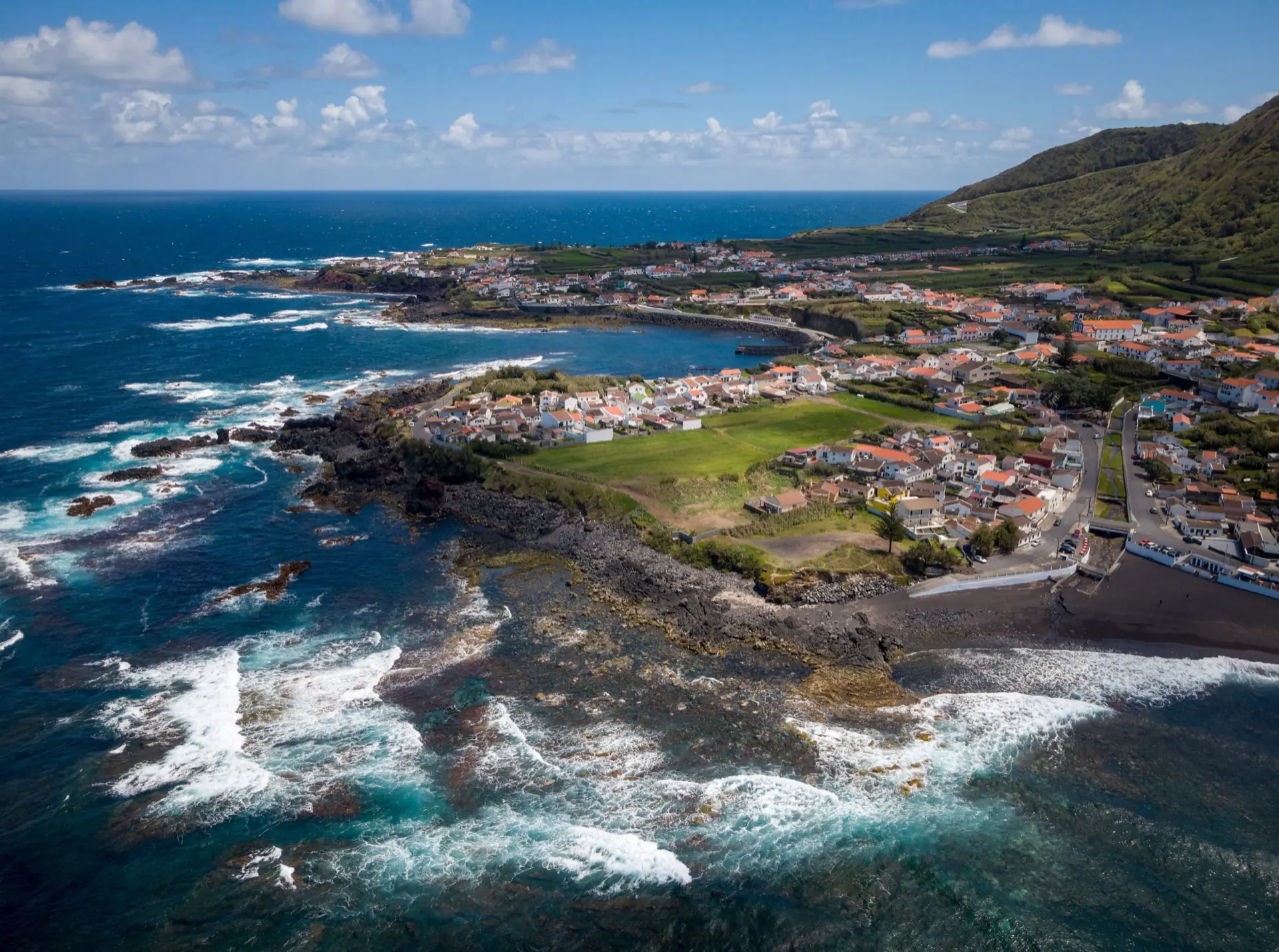 Luftaufnahme von Mosteiros an der Westküste von São Miguel: Lavaküste, schwarzer Sandstrand und weiße Häuser mit roten Dächern